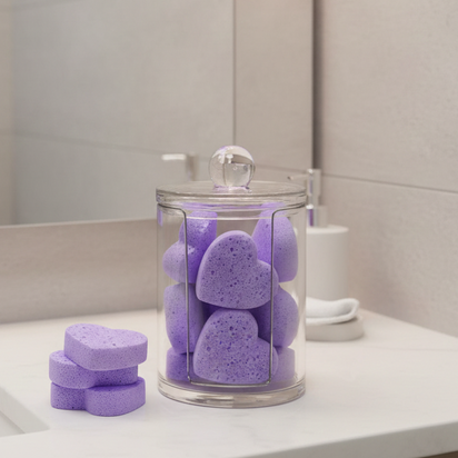 Purple heart-shaped makeup remover sponges in a glass jar on a bathroom counter.